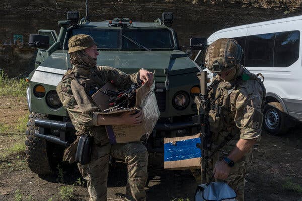 Soldati in piedi con scatole di dispositivi elettronici e strumenti specializzati davanti a veicoli militari.