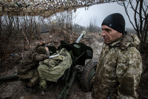Soldati vestiti in mimetica davanti a una batteria di artiglieria.